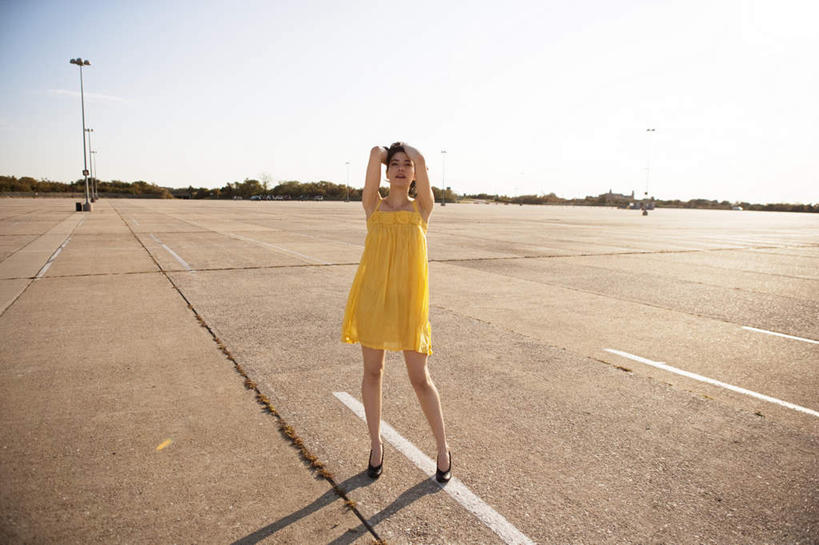 西方人,一个人,停车场,站,笑,微笑,横图,室外,白天,正面,裙子,路灯,照明,欧洲,欧洲人,仅一个年轻女性,仅一个女性,仅一个人,阴影,连衣裙,光线,界线,线条,影子,灯光,分界线,地面,注视,灯,黄色,蓝色,蓝天,天空,阳光,天,观察,看,站着,晴朗,观看,照亮,察看,双手抱头,照明设备,关注,万里无云,年轻女性,女人,女性,白种人,晴空,晴空万里,站立,彩图,全身,泊车场