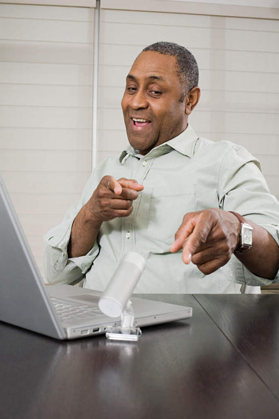 西方人,一个人,坐,笑,微笑,露齿笑,竖图,室内,白天,正面,电脑,笔记本电脑,桌面,桌子,欧洲,非洲,黑人,欧洲人,仅一个男性,仅一个人,仅一个中年男性,指,服装,时间,网络,木制,时钟,手表,摄像机,计时,注视,指点,休闲装,通讯设备,衣服,木制品,钟表,观察,看,休闲,休闲服,表,摄像,摄影,服饰,摄影机,观看,腕表,察看,无线,指向,关注,录像,通信设备,无线网络,无线上网,便携式电脑,手提电脑,男人,男性,中年男性,非洲人,钟,坐着,半身,彩图