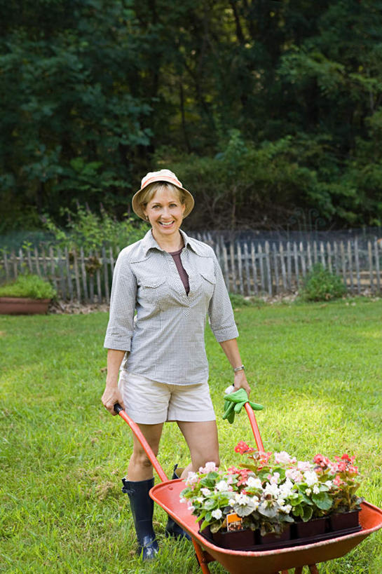 西方人,一个人,站,笑,微笑,露齿笑,竖图,室外,白天,正面,安全,草地,草坪,植物,帽子,鞋子,欧洲,欧洲人,仅一个女性,仅一个人,一辆,握,阴影,服装,盛开,光线,草帽,影子,雨鞋,雨靴,防护,拿,花蕾,拿着,注视,休闲装,靴子,车,草,花,花瓣,花朵,鲜花,树,树木,衣服,绿色,阳光,自然,手套,手推车,交通工具,花苞,花蕊,观察,看,站着,仅一个中年女性,休闲,休闲服,握着,服饰,独轮车,生长,成长,观看,保护,察看,关注,载具,胶鞋,保险,保全,周全,安稳,安定,防护手套,平安,女人,女性,中年女性,白种人,站立,彩图,全身