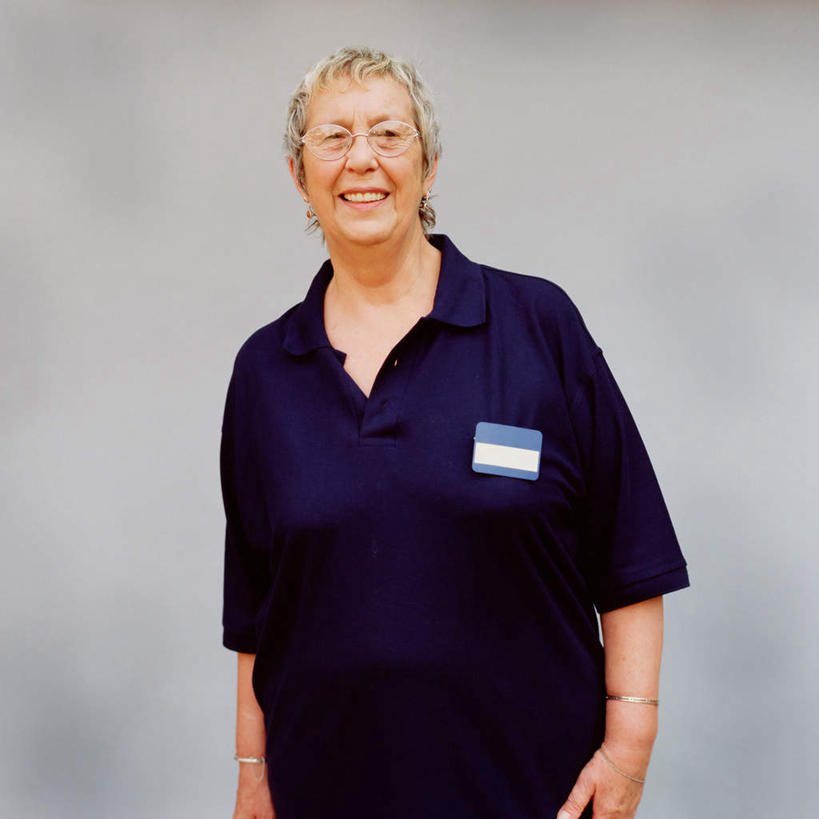 西方人,一个人,站,笑,微笑,露齿笑,方图,室内,白天,正面,工作服,制服,欧洲,欧洲人,仅一个女性,仅一个人,一副,灰色背景,眼镜,注视,标识,吊牌,一个,蓝色,胸牌,观察,看,站着,仅一个中年女性,摄影,影棚,单个,观看,察看,徽章,关注,身份,销售员,近视眼镜,胸章,胸卡,编号牌,雕刻牌,工号牌,胸号牌,胸徽,员工牌,工作制服,女人,女性,中年女性,白种人,站立,半身,彩图,影棚拍摄,工作套服,拍摄