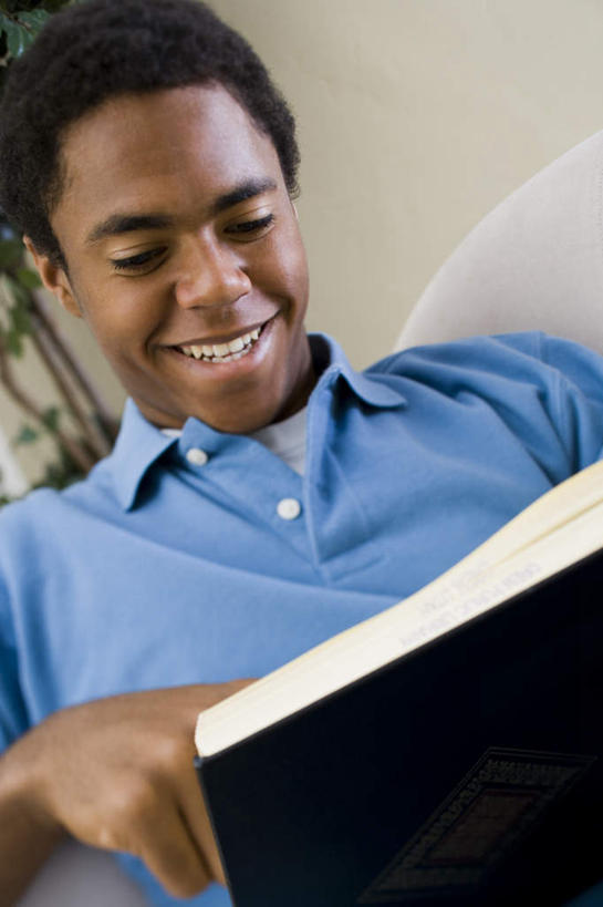 西方人,一个人,客厅,坐,笑,微笑,露齿笑,竖图,室内,白天,正面,植物,沙发,书籍,欧洲,非洲,黑人,欧洲人,仅一个男性,仅一个人,一本,握,服装,盆栽,盆景,拿,拿着,注视,休闲装,树,树木,仅一个年轻男性,衣服,蓝色,绿色,自然,观察,看,休闲,休闲服,握着,服饰,生长,成长,观看,察看,起居室,关注,布艺沙发,客堂,男人,男性,年轻男性,非洲人,书,图书,坐着,半身,彩图