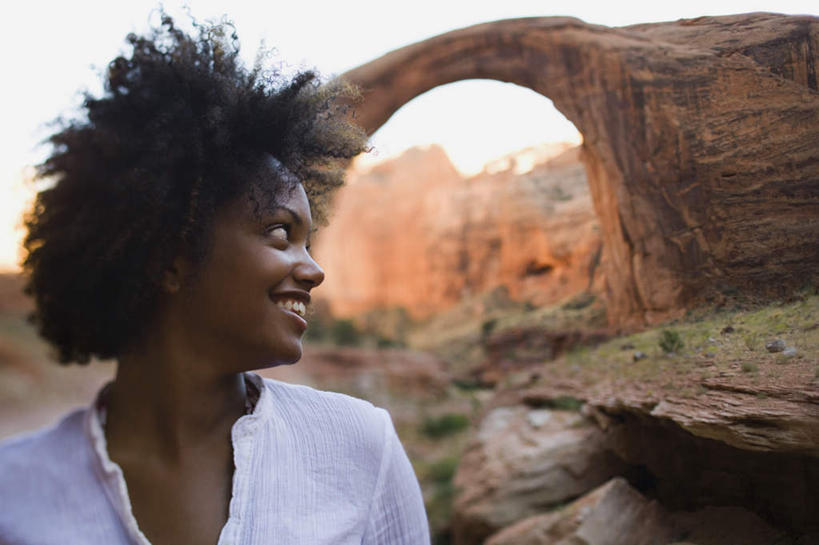 西方人,脸,头,脸颊,脖子,一个人,站,笑,微笑,露齿笑,横图,室外,白天,正面,草地,石头,山,山脉,植物,欧洲,非洲,黑人,欧洲人,仅一个年轻女性,仅一个女性,仅一个人,服装,朦胧,模糊,石子,山峰,拱门,山峦,扭头,注视,休闲装,肩膀,草,衣服,绿色,白色,群山,观察,看,站着,转头,休闲,休闲服,服饰,观看,察看,关注,沉积岩,水成岩,年轻女性,女人,女性,非洲人,头部,脖,颈,颈部,脸部,脸蛋,面部,石块,岩石,站立,半身,彩图