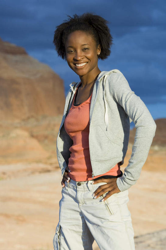 西方人,一个人,站,笑,微笑,露齿笑,竖图,室外,白天,正面,石头,山,山脉,欧洲,非洲,黑人,欧洲人,仅一个年轻女性,仅一个女性,仅一个人,阴影,服装,光线,石子,影子,山顶,山峰,云,云朵,山峦,云彩,注视,休闲装,手叉腰,衣服,蓝色,白云,蓝天,天空,阳光,群山,天,叉腰,观察,看,站着,休闲,休闲服,服饰,晴朗,观看,察看,关注,沉积岩,颠峰,极峰,水成岩,年轻女性,女人,女性,非洲人,石块,岩石,晴空,站立,半身,彩图