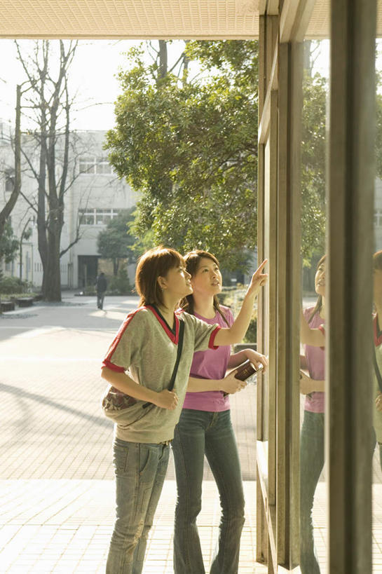 东方人,两个人,伙伴,朋友,站,竖图,室外,白天,侧面,友谊,窗户,亚洲,指,服装,拿,拿着,注视,休闲装,黄种人,方向,玻璃窗,衣服,观察,看,手势,站着,休闲,休闲服,服饰,观看,察看,指向,关注,宣传栏,通告栏,友情,年轻女性,女人,女性,亚洲人,站立,半身,彩图