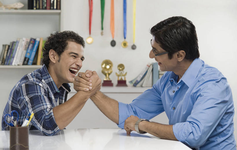 两个人,家庭,父亲,儿子,坐,笑,微笑,大笑,露齿笑,横图,室内,白天,侧面,游戏,兴奋,成功,胜利,比赛,桌面,桌子,书籍,笔筒,亚洲,五个,许多,修剪,阴影,服装,朦胧,模糊,时间,反射,工具,剪刀,时钟,手表,眼镜,影子,墙,大理石,玩,计时,注视,休闲装,右手,娱乐,相视,墙壁,墙面,两个,衣服,白色,容器,书柜,钟表,观察,看,张嘴,休闲,温暖,温馨,父子,一家人,面对面,休闲服,表,器皿,书橱,父爱,光彩,力量,扳手腕,服饰,观看,活动,储藏,对视,裁剪,腕表,和睦,察看,剪子,剪裁,切割,掰手腕,互视,储存,发泄,关注,消遣,智力,奖牌,相对,荣誉,奖品,近视眼镜,张大嘴巴,相看,哈哈大笑,宣泄,荣耀,大理石制品,比力,较劲,扳手劲,手肘,插笔器具,文房用具,光荣,较量,男人,男性,年轻男性,中年男性,亚洲人,印度人,胳膊,手臂,书,图书,钟,张开嘴,玩耍,嬉戏,坐着,半身,彩图,高兴,狂笑,融洽,贮存,奖杯